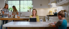 Woman is working on her laptop at a kitchen counter with kids in the background